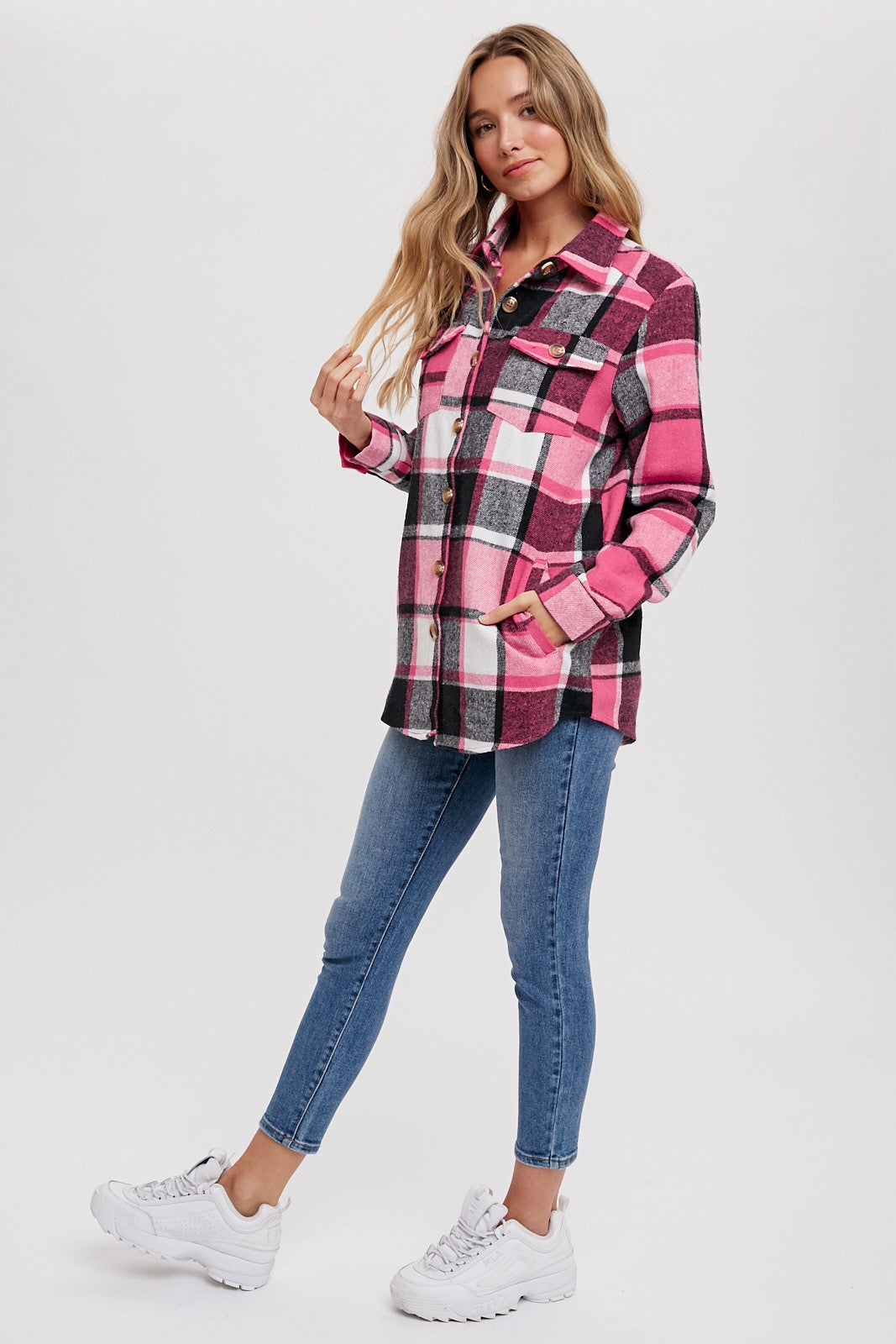 woman wearing a pink and black plaid shacket with white accents and blue skinny jeans, styled with white sneakers