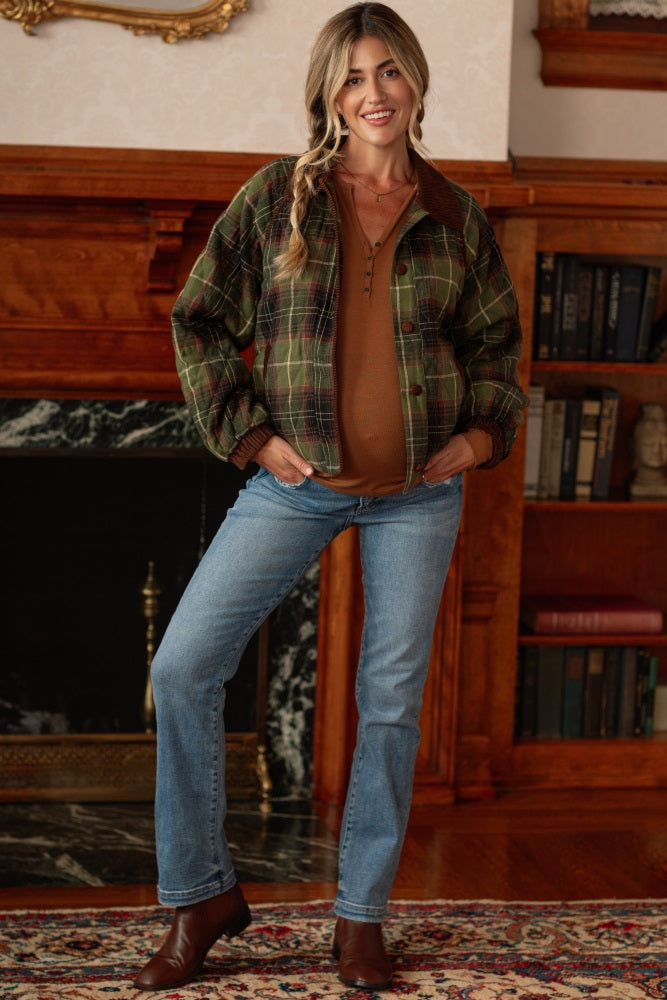 woman wearing a green and brown plaid maternity jacket over a mustard long sleeve top and blue jeans, with a visible baby bump
