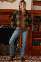 woman wearing a green and brown plaid maternity jacket over a mustard long sleeve top and blue jeans, with a visible baby bump