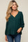 woman wearing a dark green maternity top with a v-neck and long sleeves, smiling and standing with hands on her belly