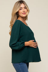 woman wearing a dark green maternity top with a v-neck and balloon sleeves, holding her baby bump