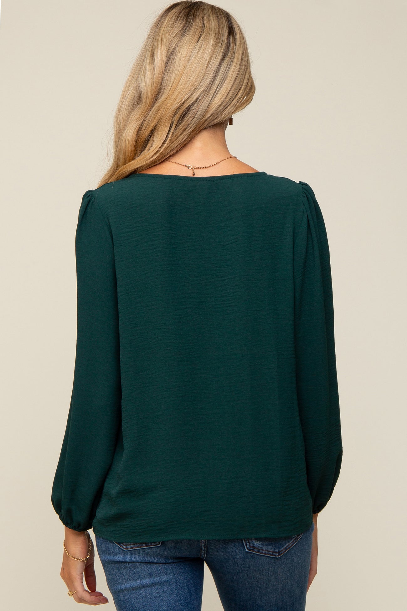 woman wearing a dark green maternity top with balloon sleeves, displaying the back view