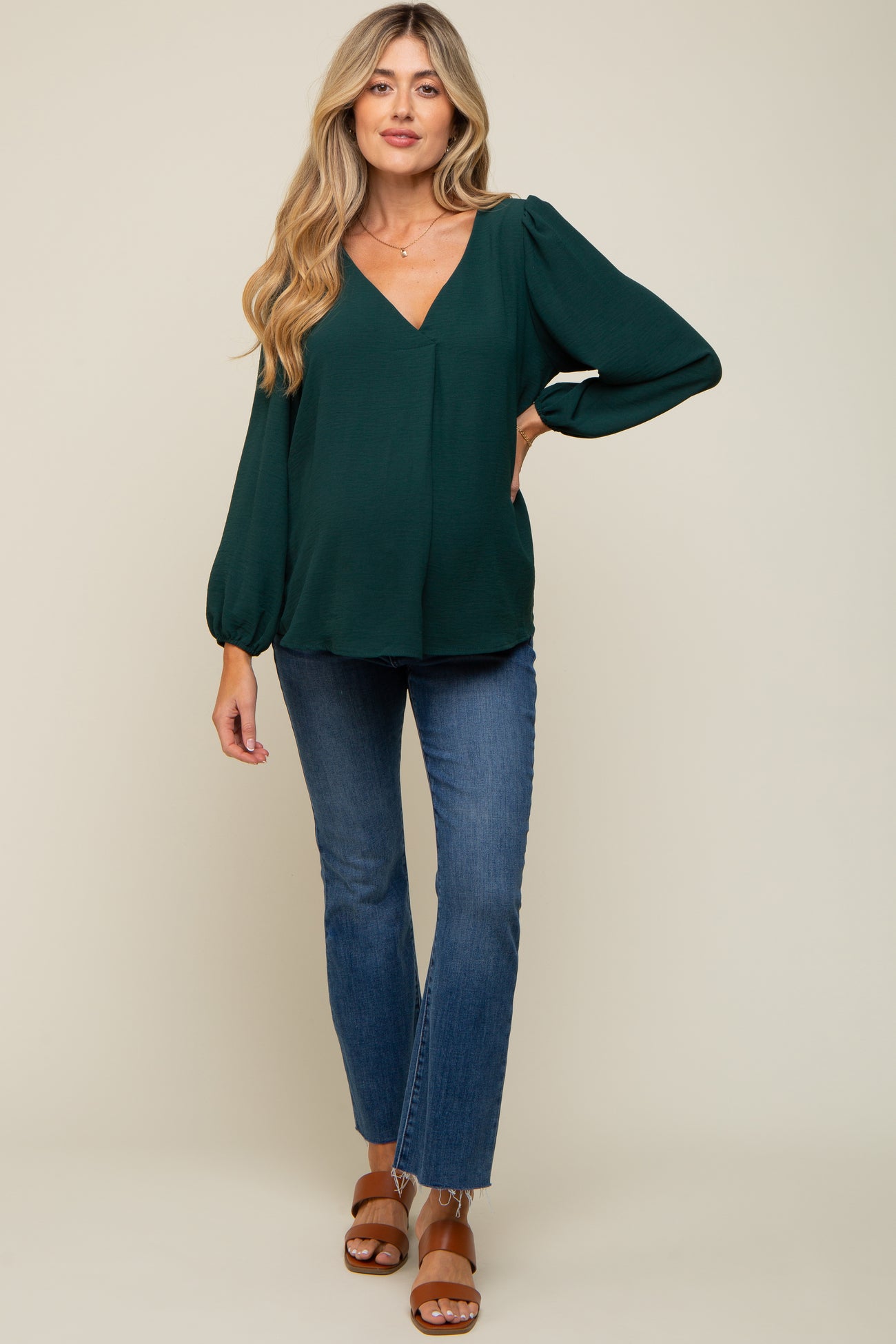 woman wearing a dark green maternity top with a v-neck and puff sleeves paired with blue flared jeans