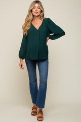 woman wearing a dark green maternity top with a v-neck and puff sleeves paired with blue flared jeans
