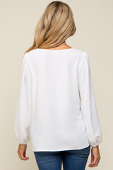 woman wearing a white long sleeve maternity top, view from the back, paired with blue jeans