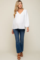 woman wearing a white long sleeve maternity top with a v-neck and jeans, showing her baby bump