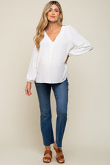 woman wearing a white v-neck maternity top with long sleeves and blue skinny jeans, showing her baby bump