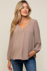 woman wearing a taupe long sleeve maternity top with a deep v-neck and puff sleeves, showcasing her baby bump