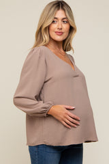 woman wearing a taupe maternity blouse with a v-neck and long puff sleeves, holding her baby bump