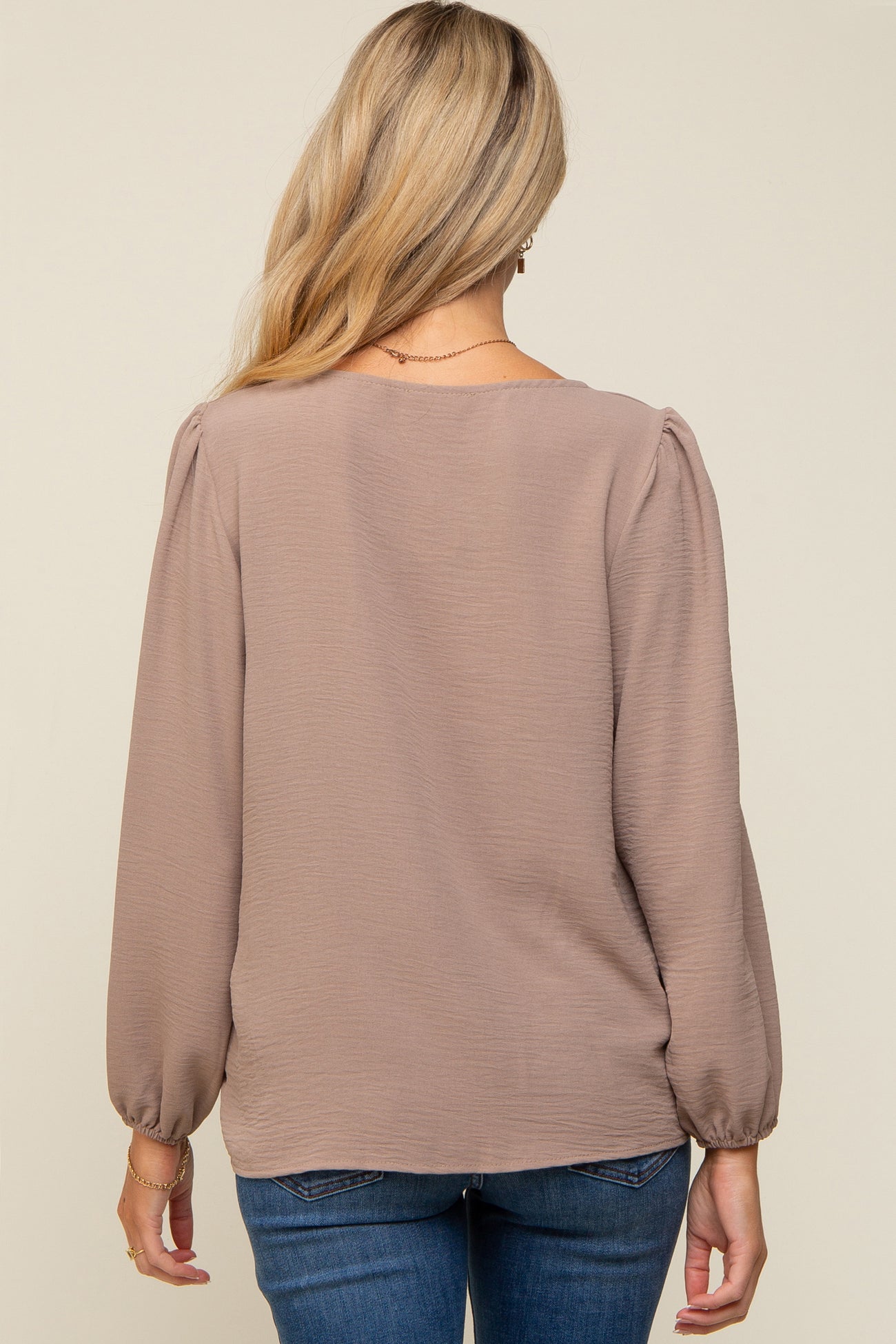 woman wearing a taupe long sleeve maternity top with puff sleeves, viewed from the back