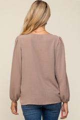 woman wearing a taupe long sleeve maternity top with puff sleeves, viewed from the back