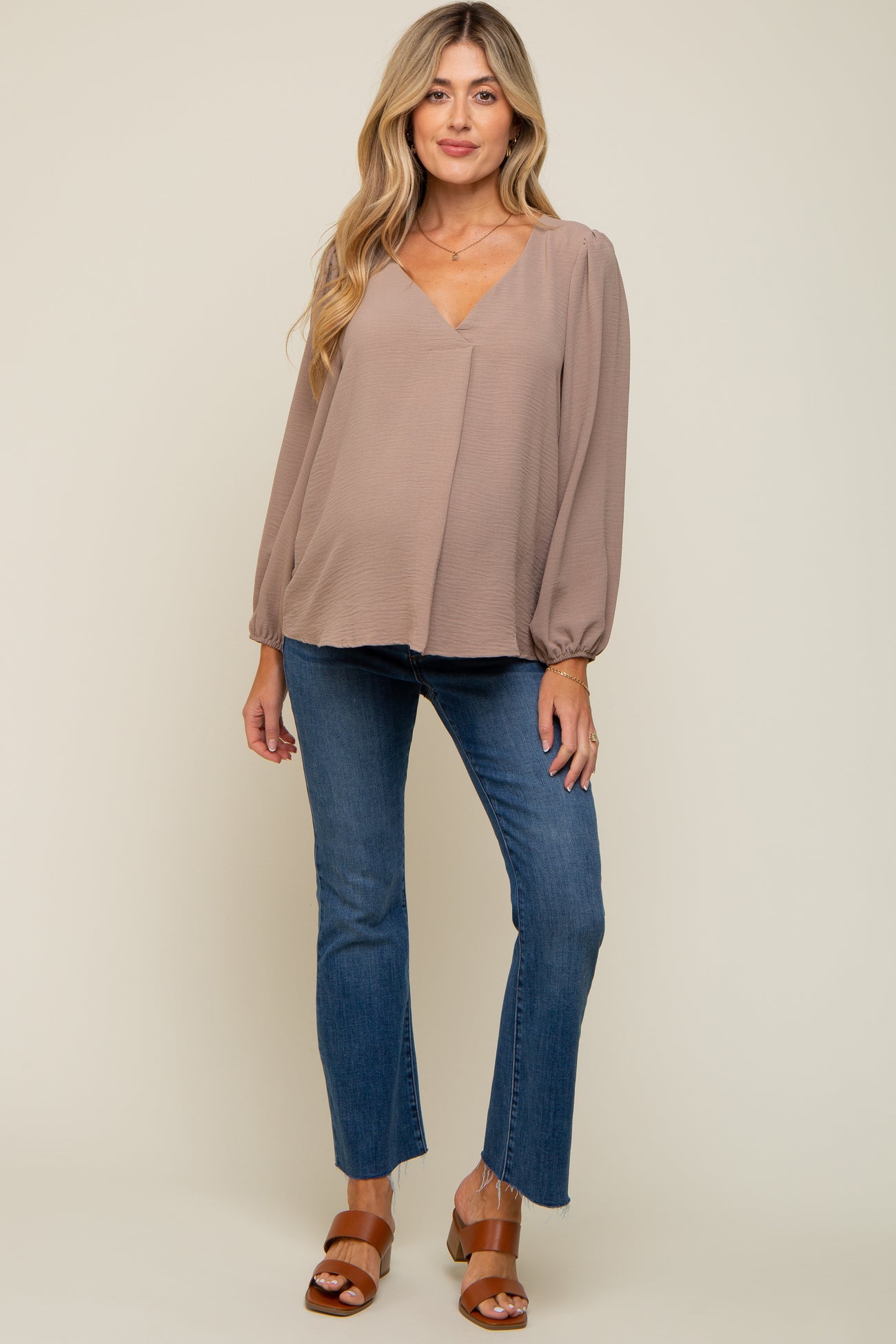 woman wearing a taupe long sleeve maternity top with a v-neckline and puff sleeves paired with flared jeans