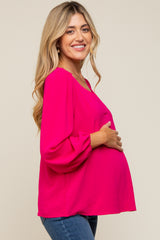 woman wearing a bright pink maternity top with puff sleeves and holding her baby bump