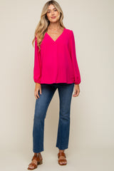 woman wearing a bright pink long sleeve maternity top and flared jeans, with loose, flowing fabric and a v-neckline