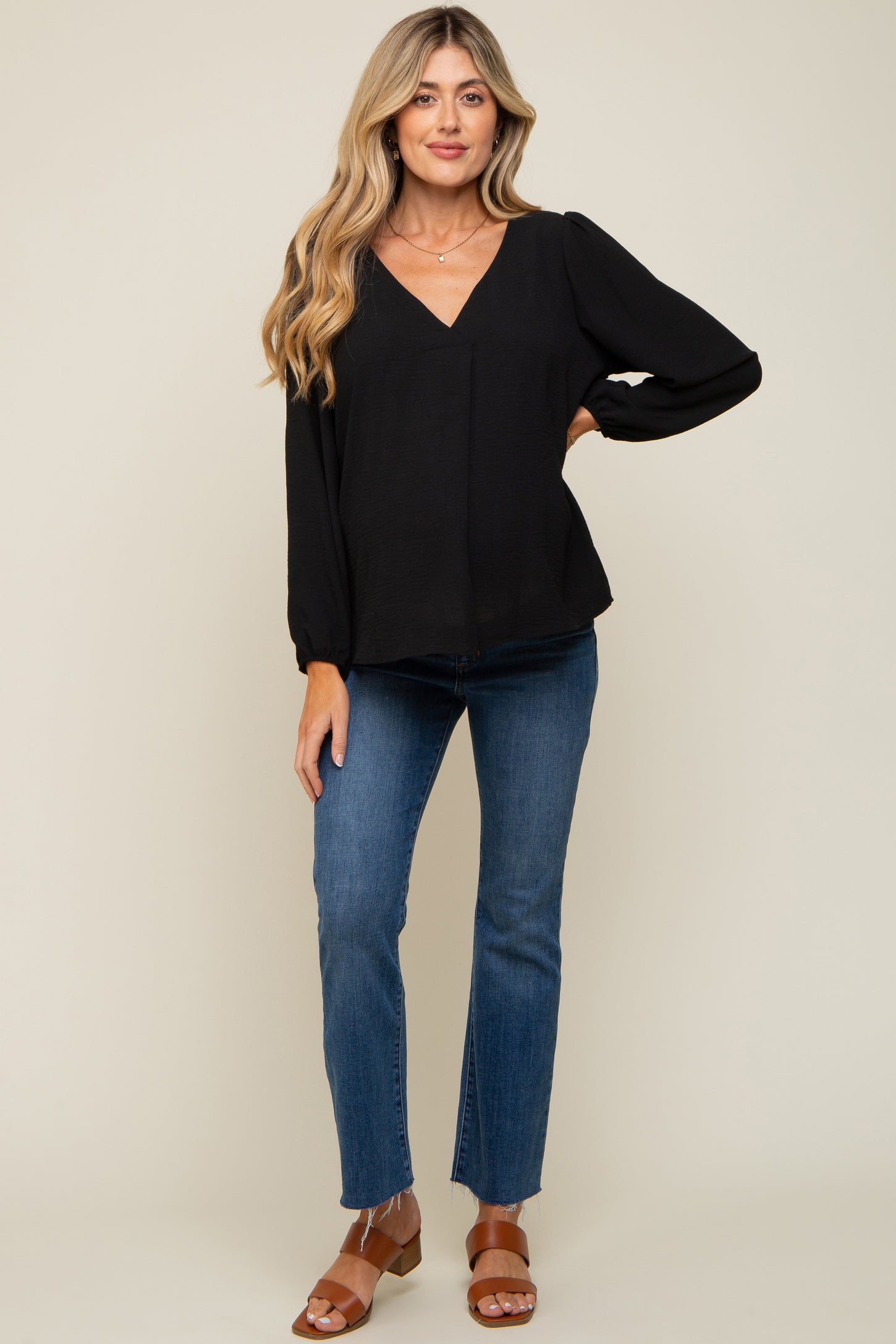 woman wearing a black maternity top with a v-neck and puff sleeves, paired with blue jeans and brown sandals