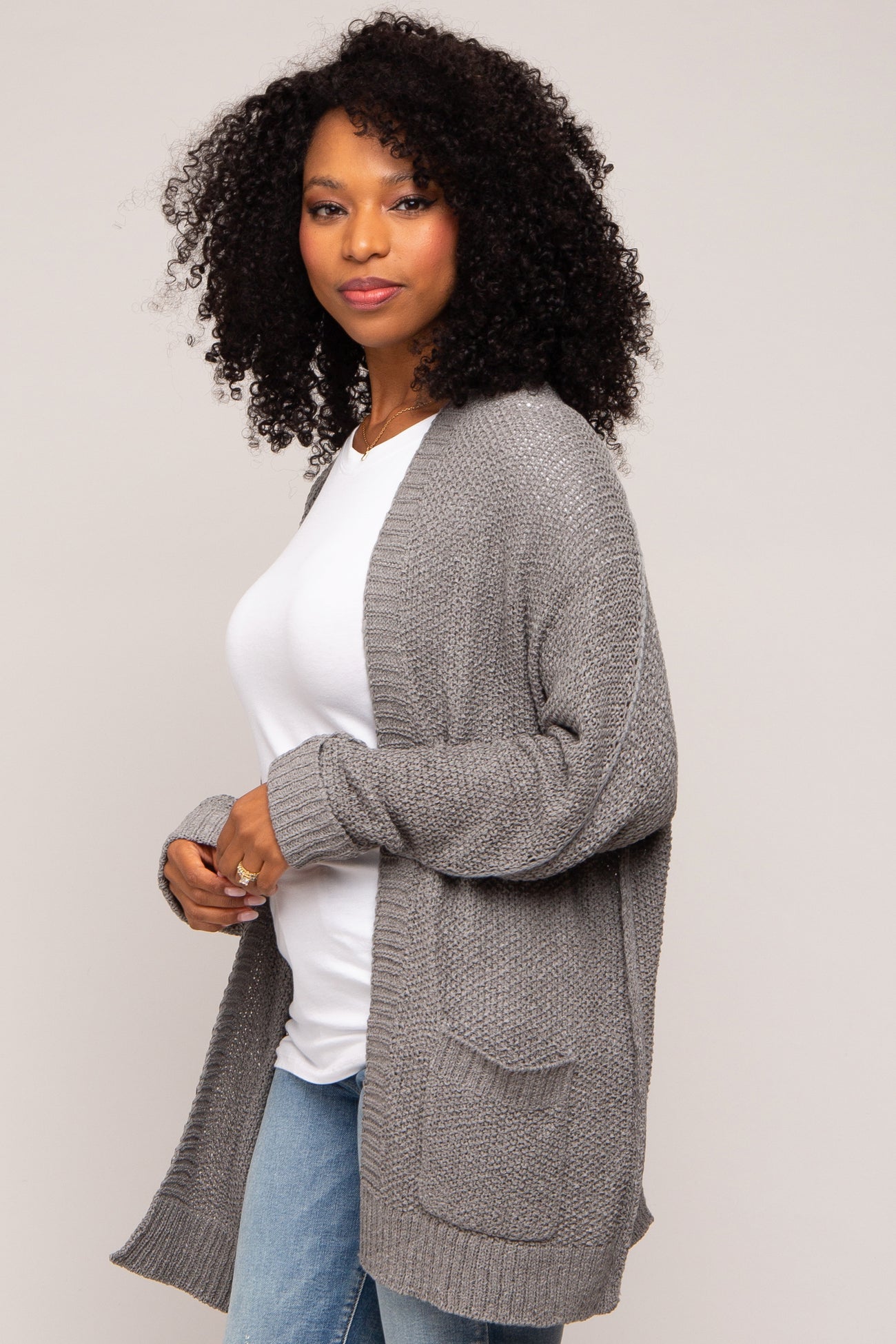 woman wearing a gray knitted cardigan over a white top and blue jeans, with curly hair styled down