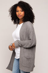 woman wearing a gray knitted cardigan over a white top and blue jeans, with curly hair styled down