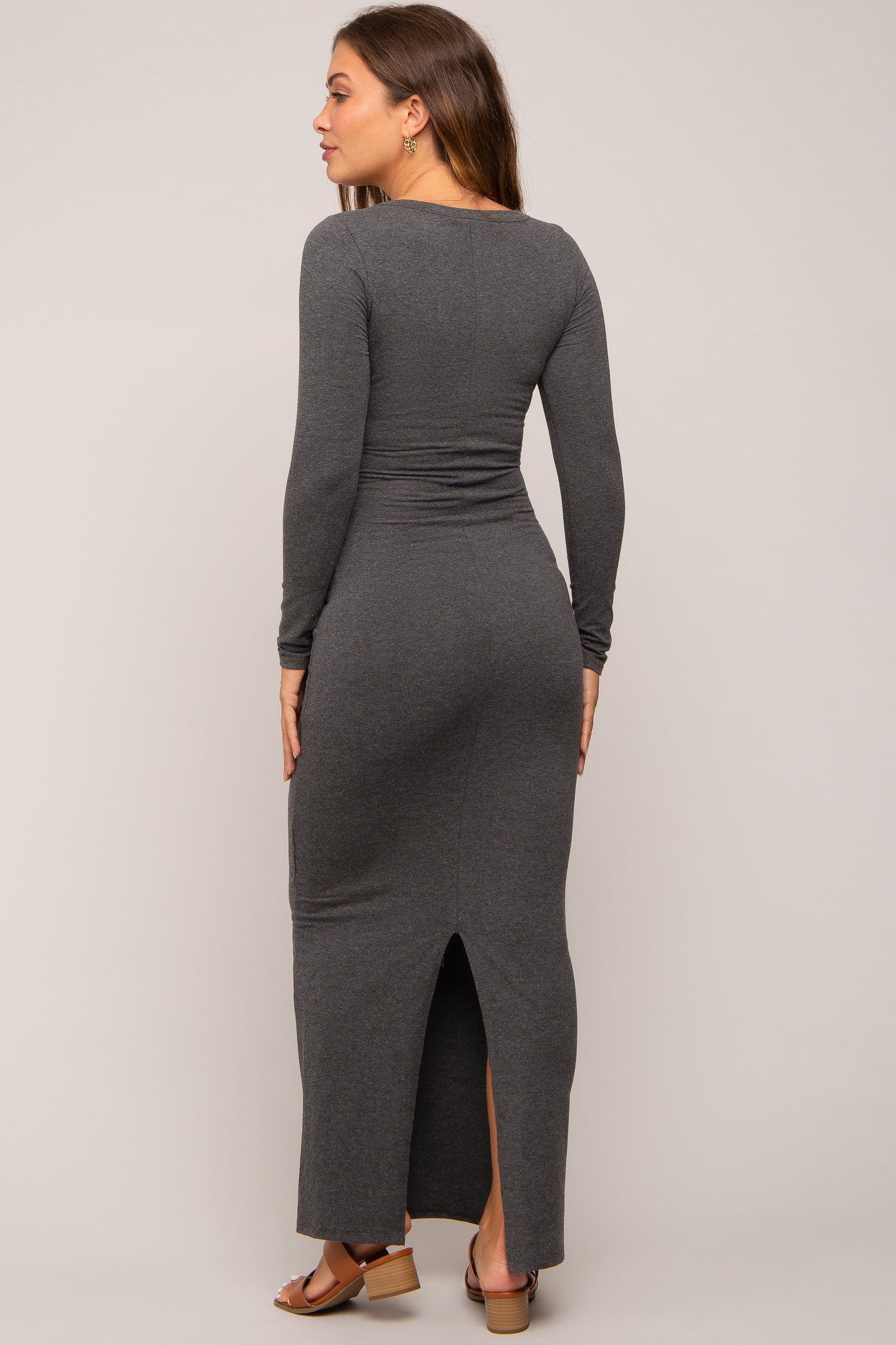 woman wearing a grey long sleeve maternity maxi dress with a back slit, displaying a baby bump