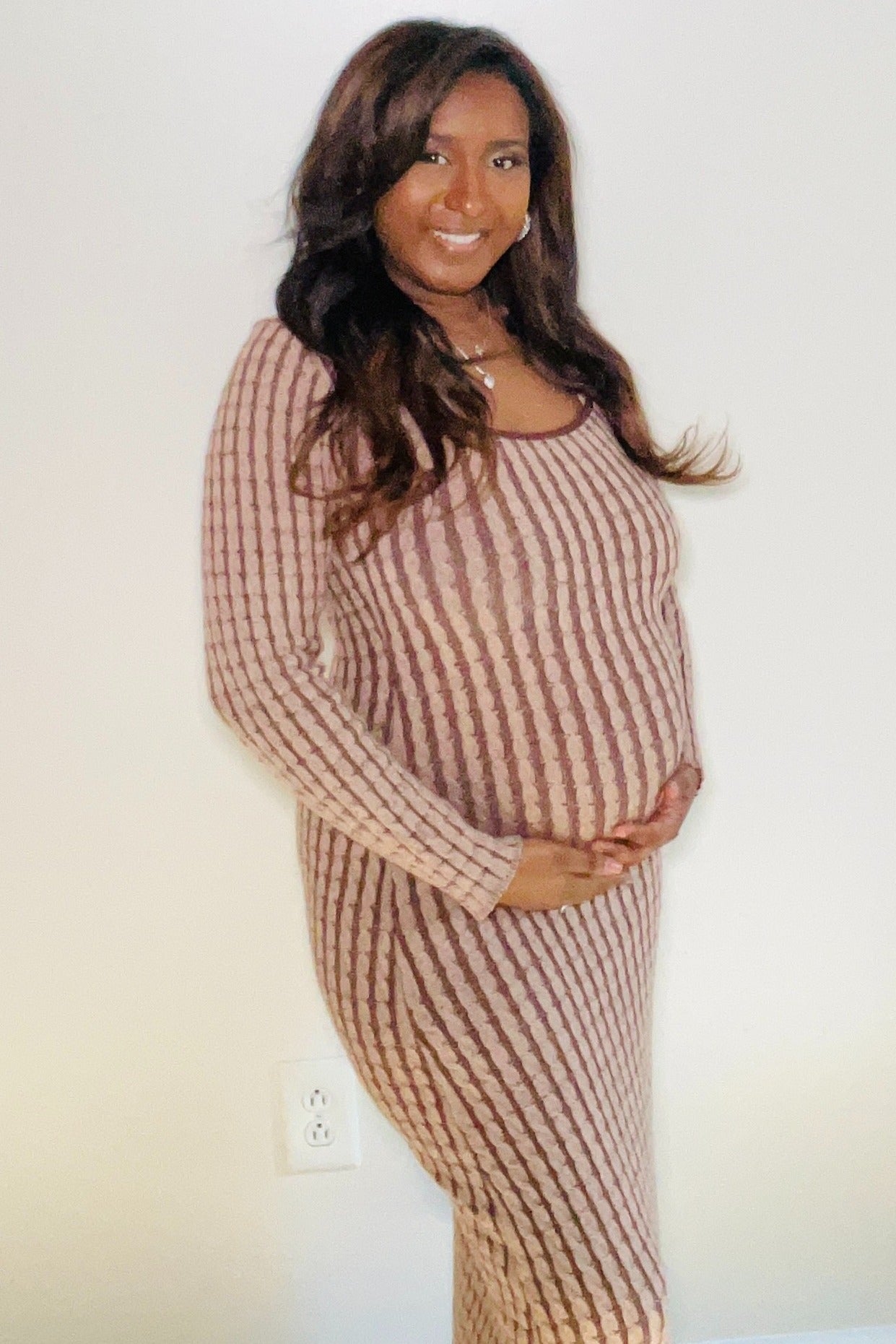 woman wearing a brown striped maternity dress and cradling her baby bump