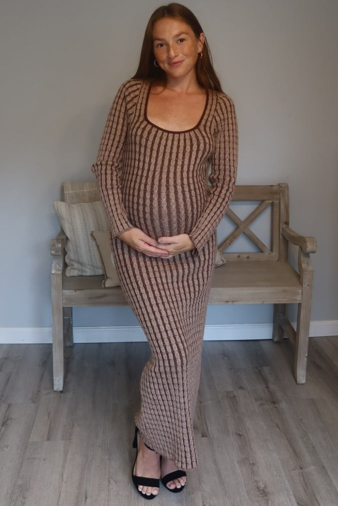 woman wearing a brown ribbed maternity dress and showing her baby bump while standing in a cozy room