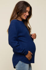 woman wearing a navy blue maternity sweater, gently cradling her baby bump, styled with light denim jeans
