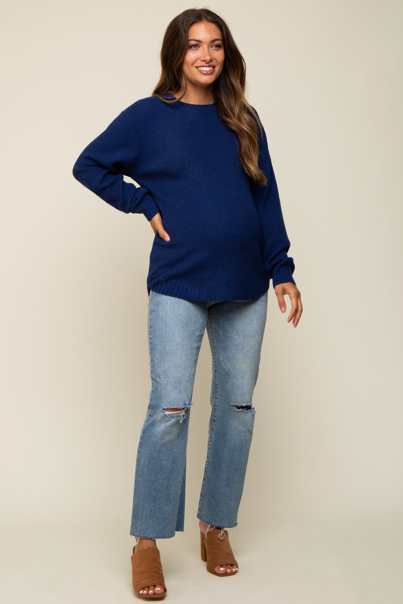 woman wearing a navy blue knit maternity sweater and light blue ripped jeans, showing her baby bump
