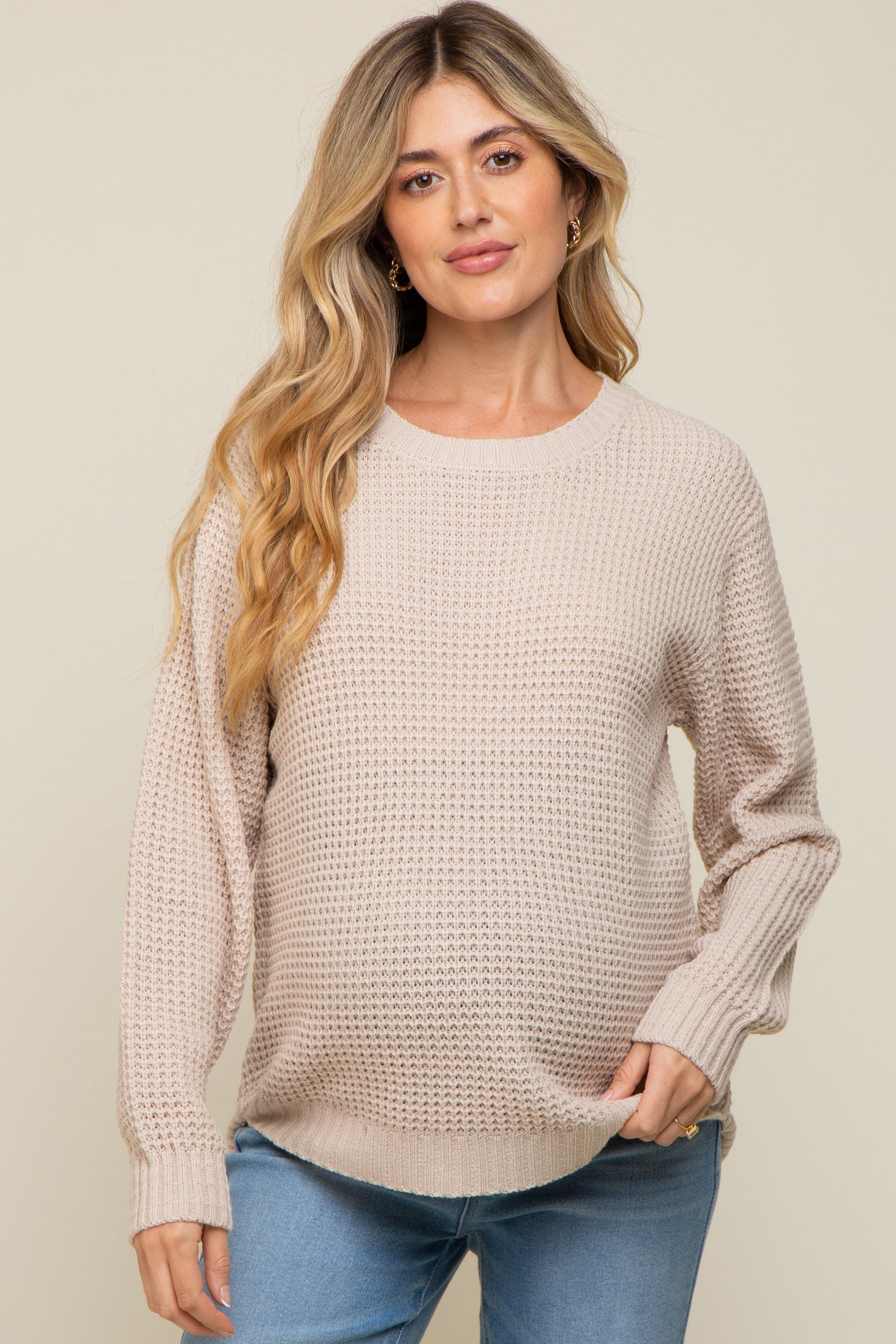 woman wearing a light beige knit maternity sweater and showing her baby bump