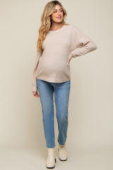 woman wearing a beige knitted maternity sweater and light blue jeans, showing off her baby bump