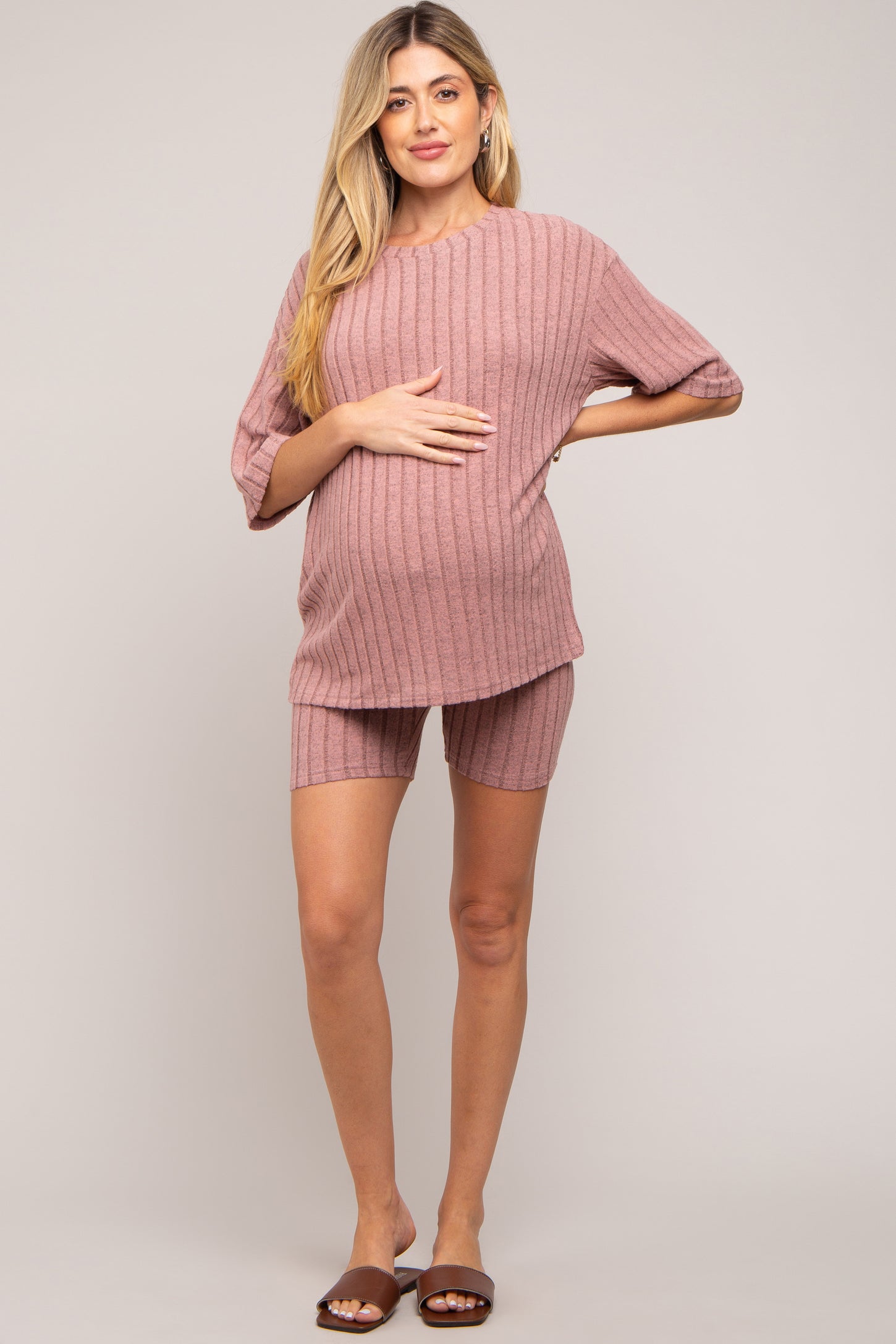 woman wearing a pink ribbed maternity loungewear set with shorts, holding her baby bump