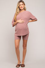woman wearing a pink ribbed maternity loungewear set with shorts, holding her baby bump