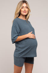 woman wearing a blue ribbed maternity two-piece set, standing with a visible baby bump and hands on her stomach