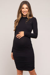 woman wearing a black long sleeve maternity dress with ruching and holding her baby bump
