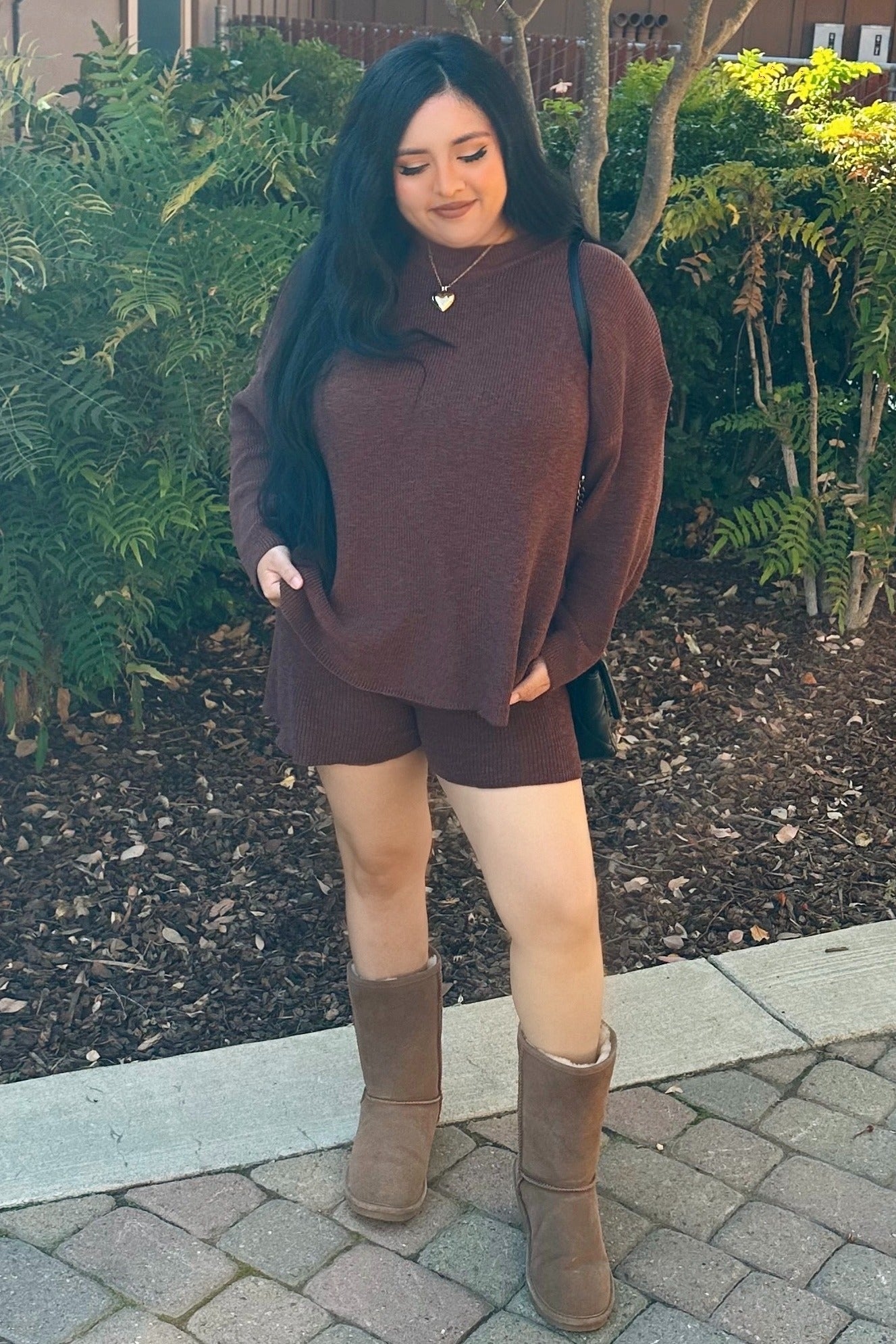 woman wearing a maroon knit sweater and shorts set with tan boots and holding a black bag