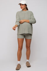 woman wearing a light green maternity sweater and shorts, showing her baby bump, with a baseball cap and slip-on shoes