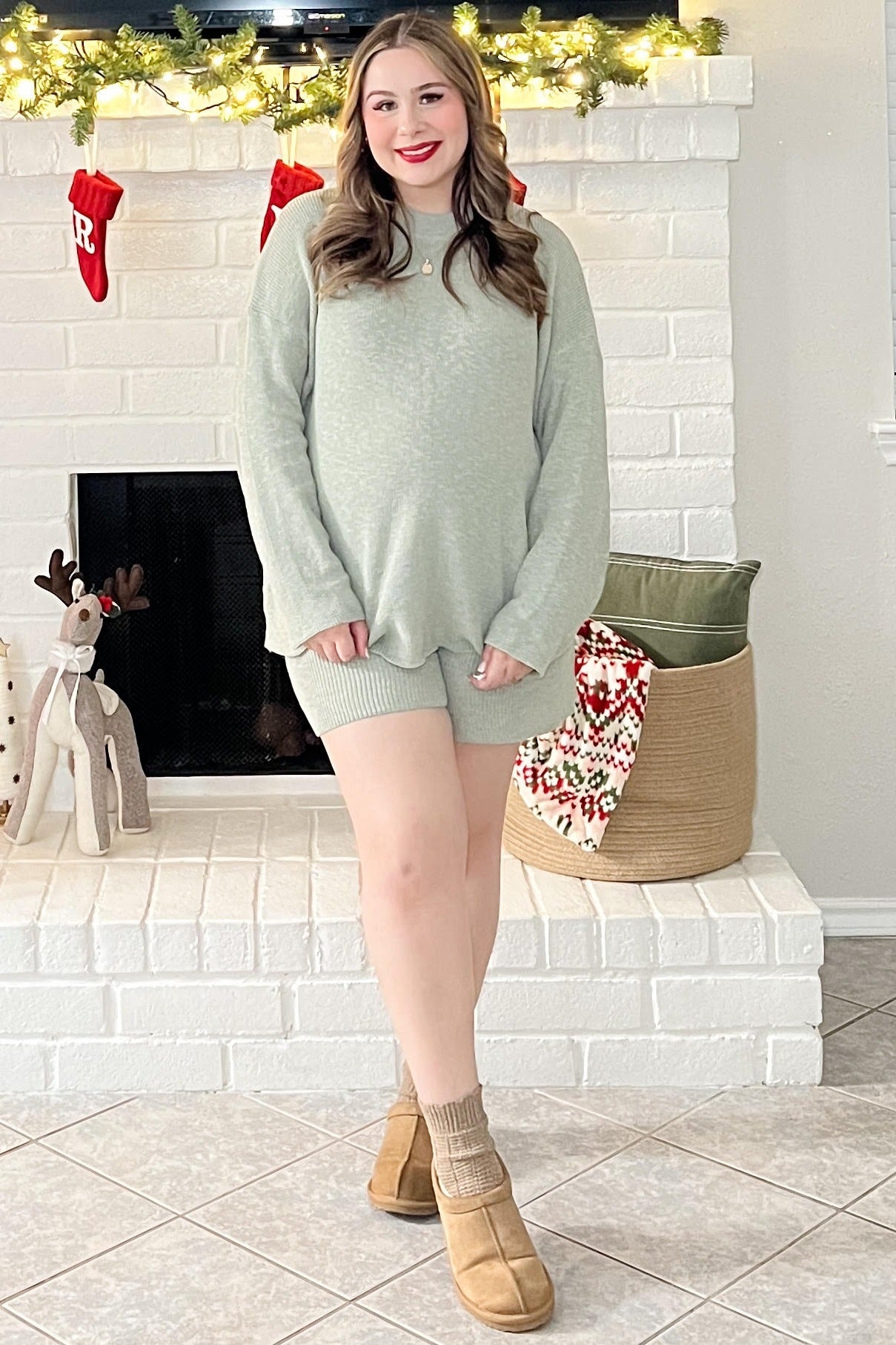 woman wearing a light green maternity loungewear set with shorts and a loose top, standing in a cozy holiday setting