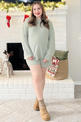 woman wearing a light green maternity loungewear set with shorts and a loose top, standing in a cozy holiday setting