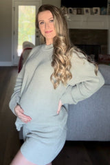 woman wearing a light green maternity sweater and shorts, showcasing her baby bump while posing indoors
