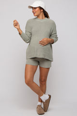 woman wearing a light green maternity sweater and matching shorts, with a visible baby bump and a white cap