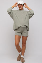 woman wearing a light green maternity sweater and matching shorts, styled with a white cap and light brown shoes