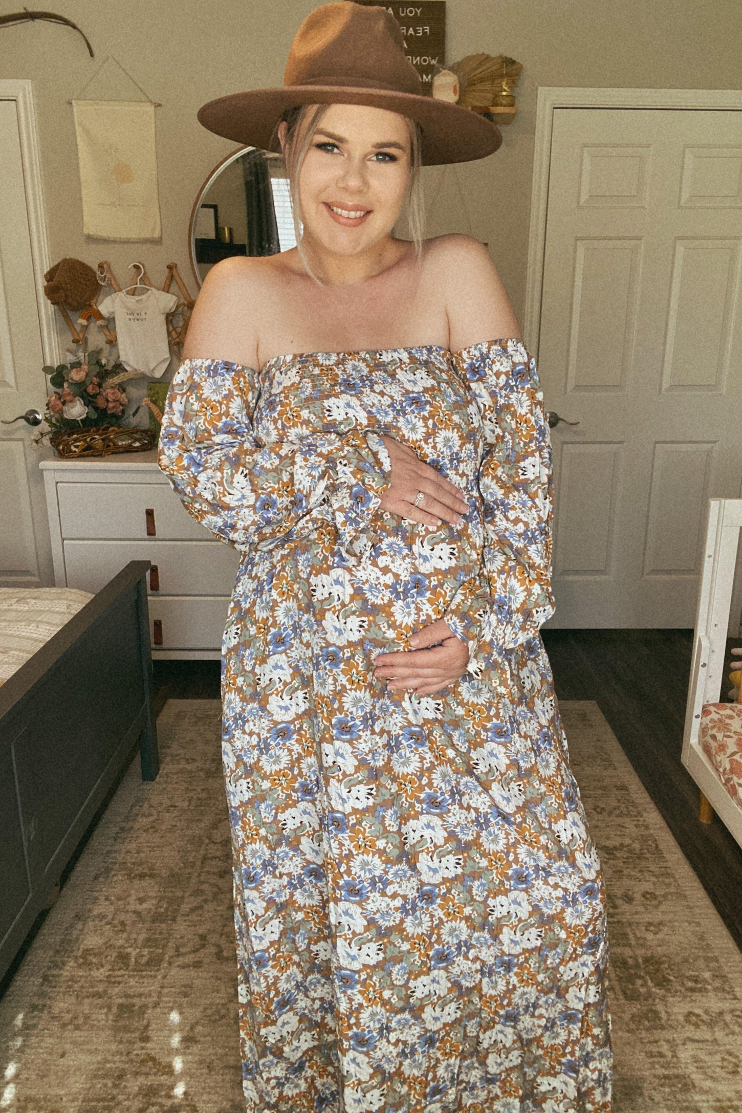 woman wearing a floral off-shoulder maternity dress and holding her baby bump