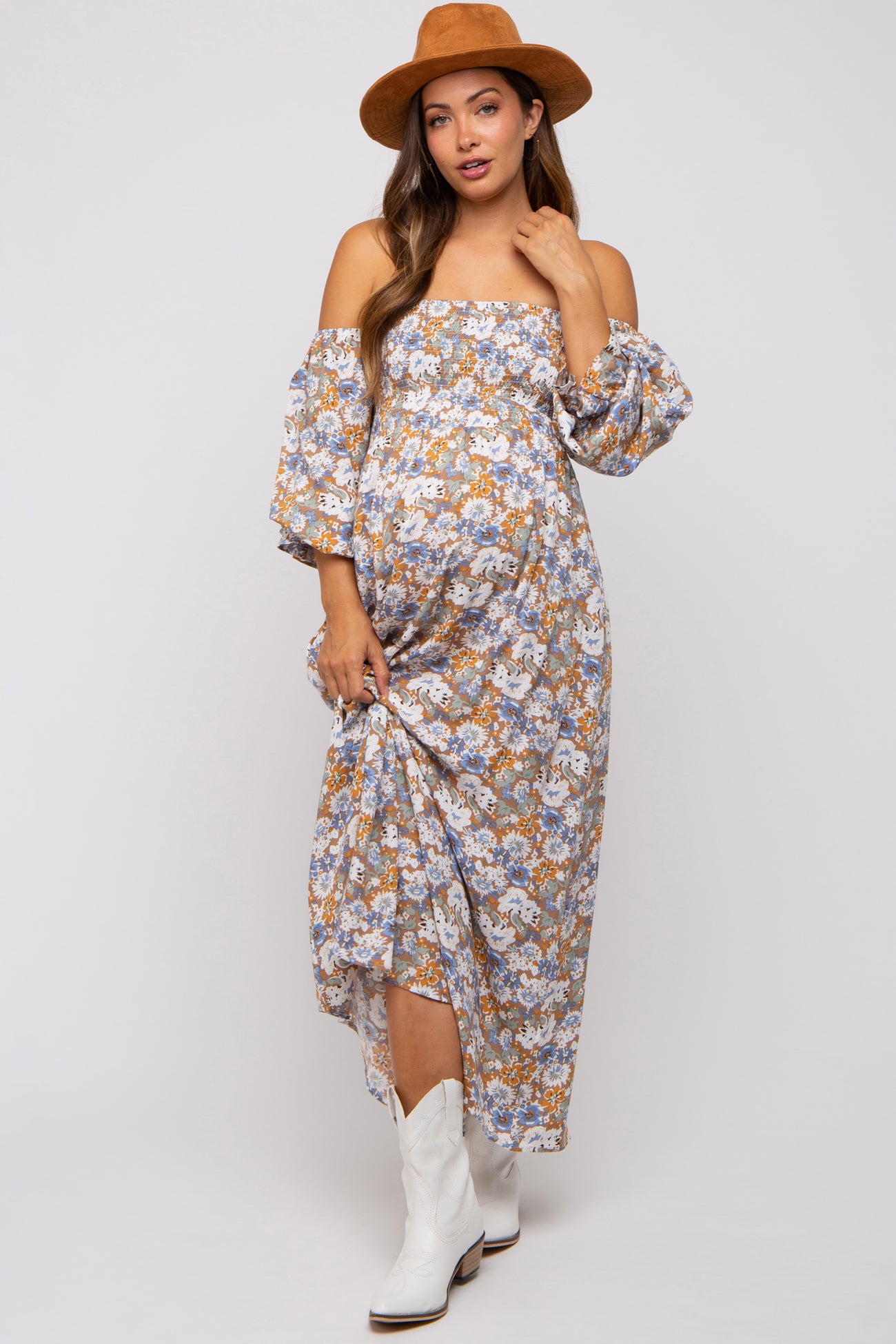 woman wearing a floral off-the-shoulder maternity dress with long sleeves and white cowboy boots, holding her baby bump