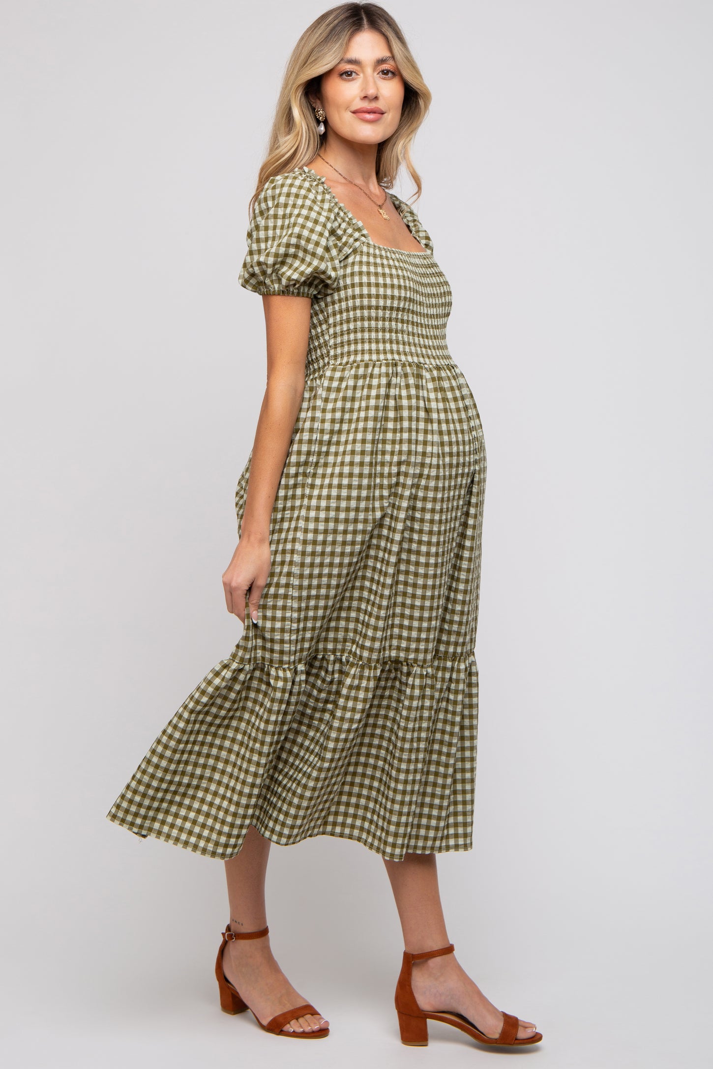 woman wearing a green and beige gingham maternity dress with puff sleeves and a tiered skirt, showing her baby bump