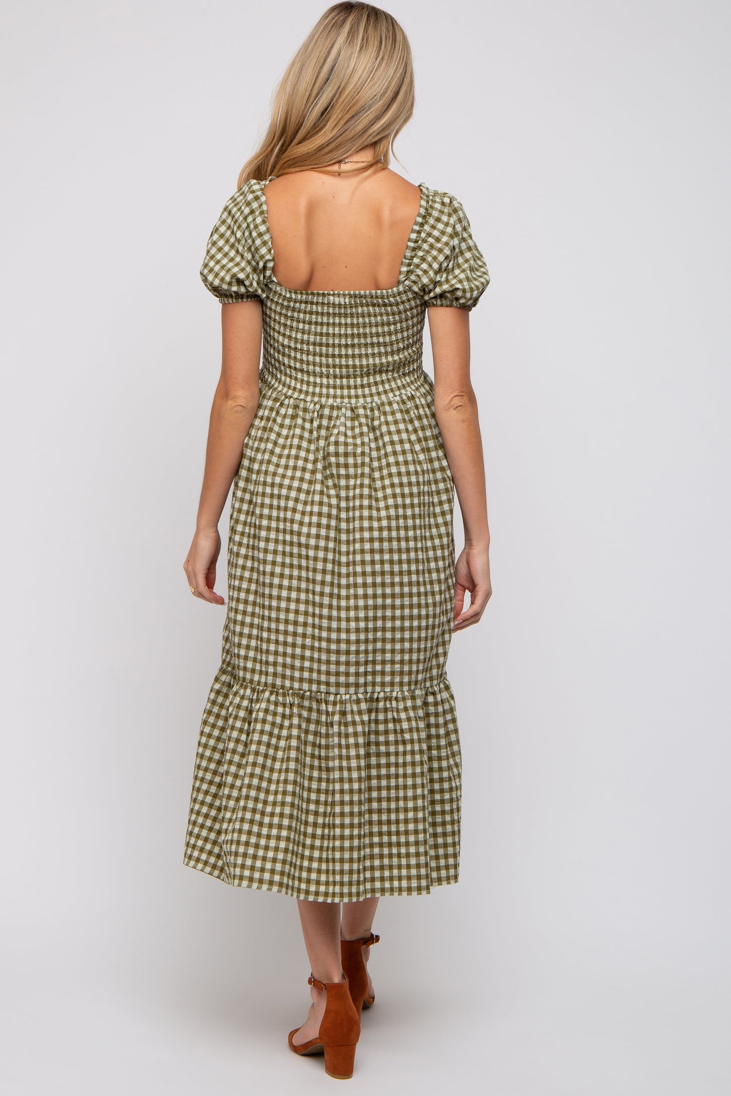woman wearing a green and white gingham maternity dress with puff sleeves and a tiered skirt, showing her baby bump