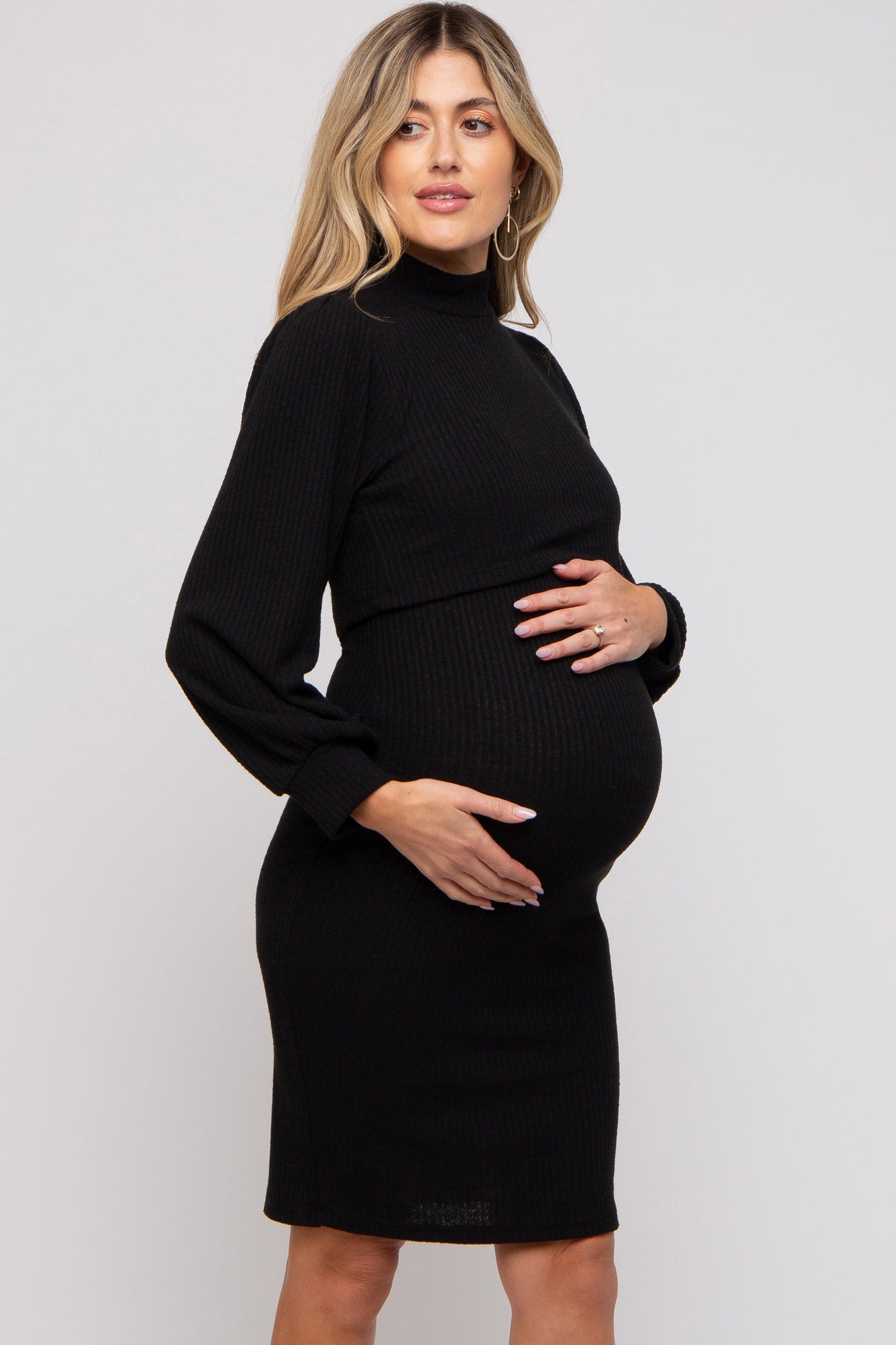 woman wearing a black ribbed maternity dress with long sleeves and a turtleneck, holding her baby bump