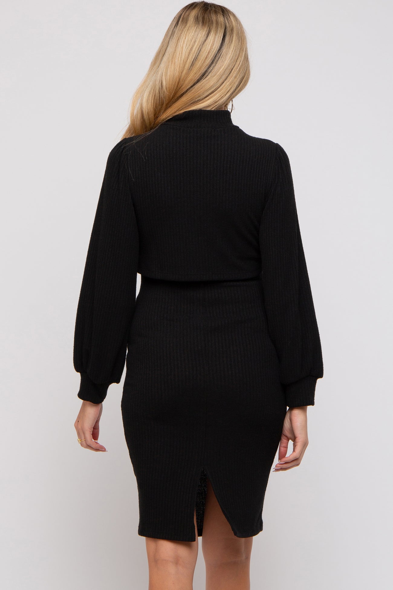 woman wearing a black ribbed maternity dress with long puff sleeves and a back slit detail