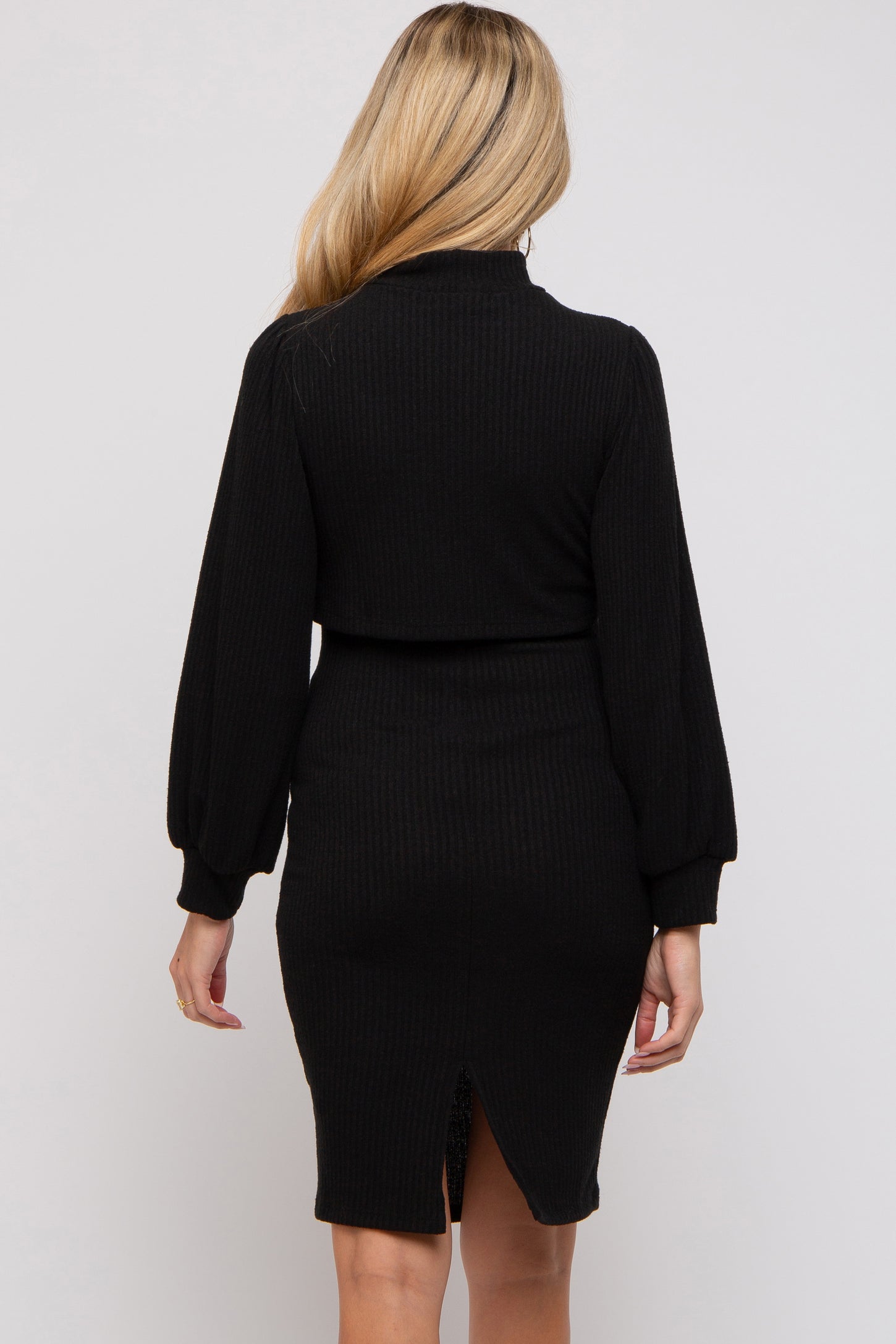 woman wearing a black ribbed maternity dress with long puff sleeves and a back slit detail