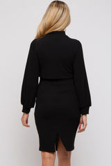 woman wearing a black ribbed maternity dress with long puff sleeves and a back slit detail