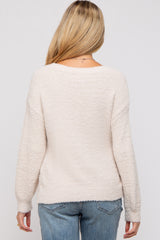 woman wearing a light beige maternity sweater with a soft texture, viewed from the back, paired with blue jeans