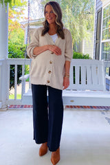 woman wearing a beige cardigan and a white tank top paired with black wide-leg pants, standing by a porch swing