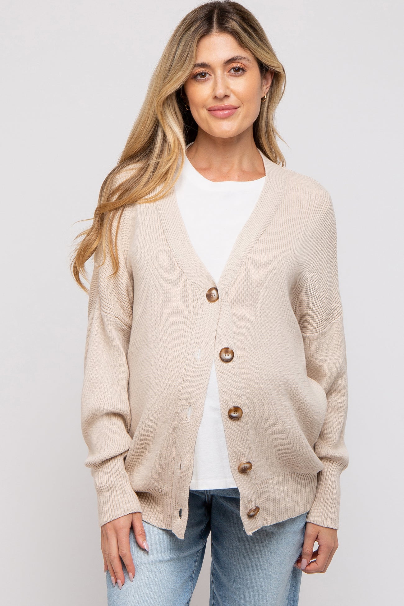 woman wearing a beige maternity cardigan with buttons, paired with a white t-shirt and blue jeans, showing a baby bump